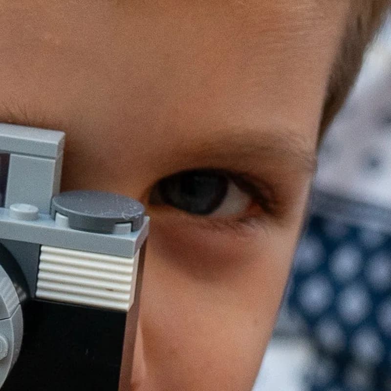 Close-up of the boy's visible eye from the same photo: the eye and lashes are soft, while the edge of the toy camera beside it is crisper.