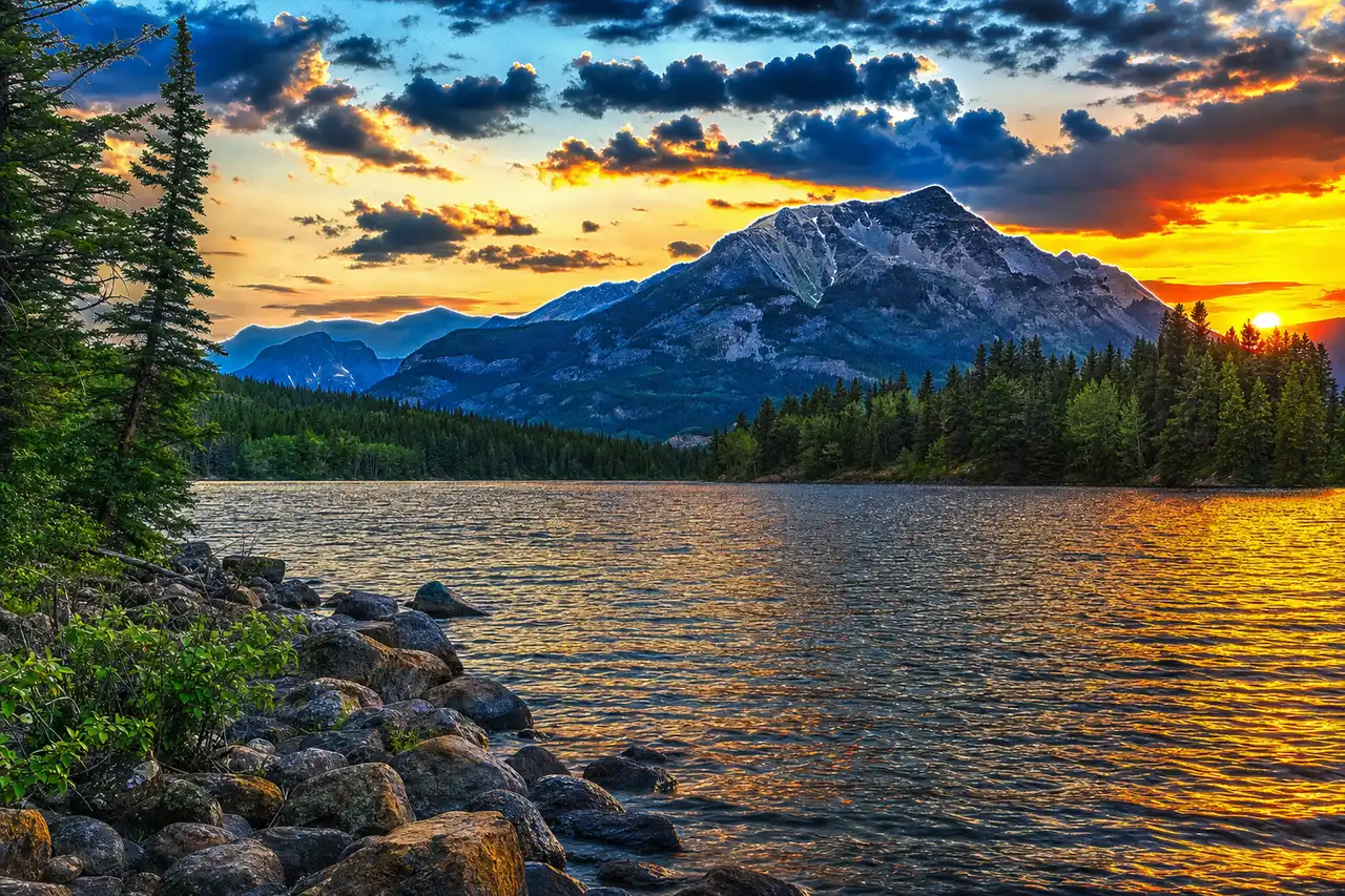 AI-generated image of an over-processed mountain-lake sunset: over-saturated colours, crunchy over-sharpened HDR detail and faint bright halos along the ridgeline (a landscape edited too hard).