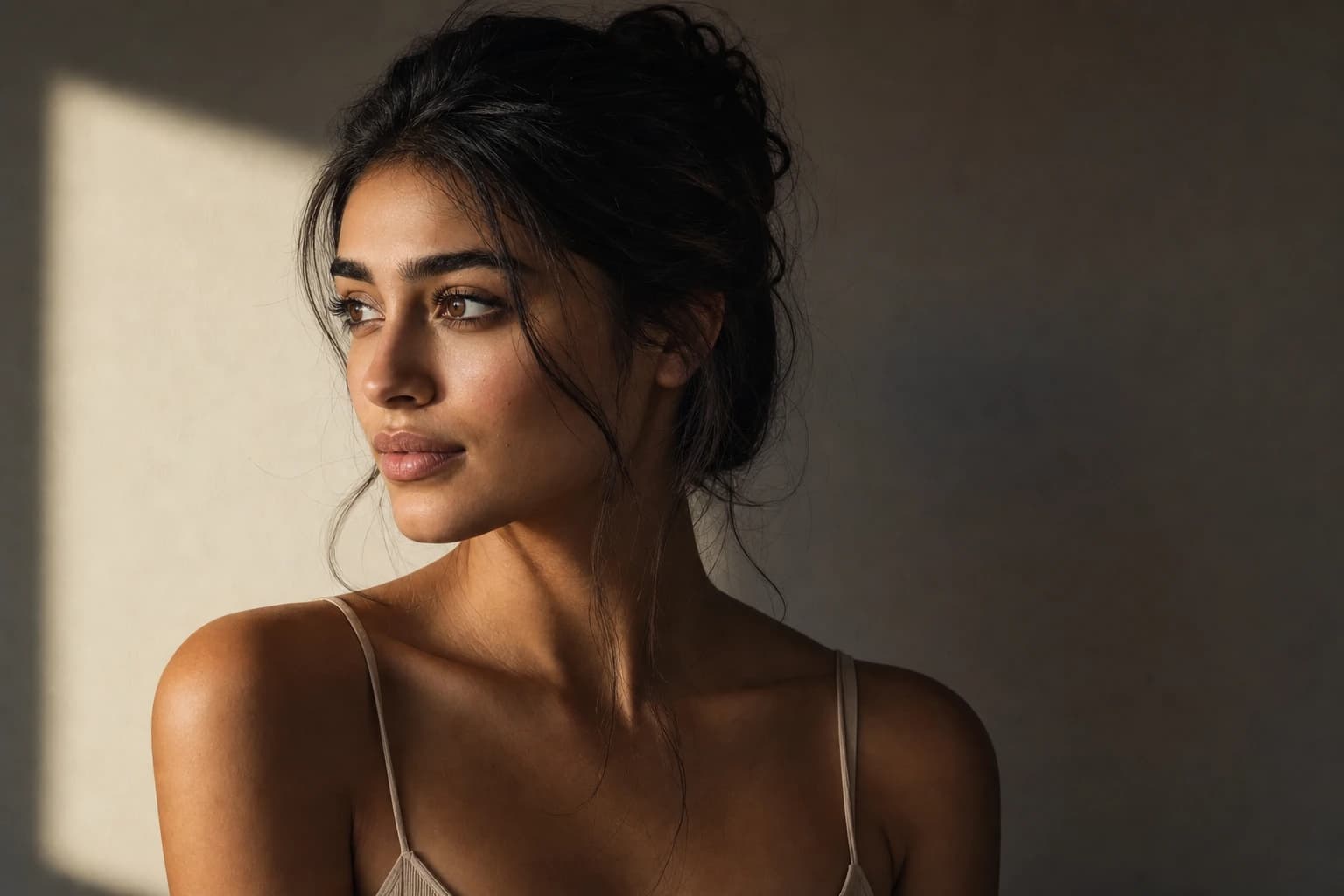 AI-generated image of a dark-haired woman lit softly from a window at the left, her face turning gradually from a warm lit cheek through smooth midtones into gentle shadow, a soft rectangle of window light on the wall behind her.
