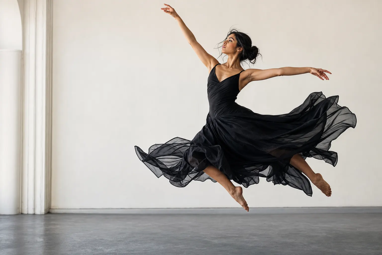 AI-generated image of a dark-haired dancer in a flowing black dress frozen at the apex of a mid-air leap in a bright studio, one arm reaching high with her gaze following it, the sheer fabric flared and suspended around her.